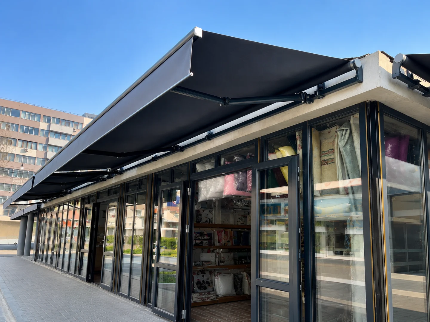Copertine retractabile cu brațe articulate și pânză închisă la culoare pe o fațadă comercială