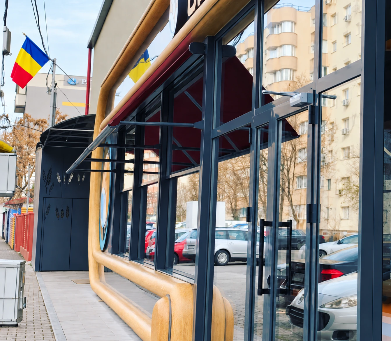 Vedere laterală a brațelor copertinelor și a fațadei vitrate Koksal, cu profile gri antracit.